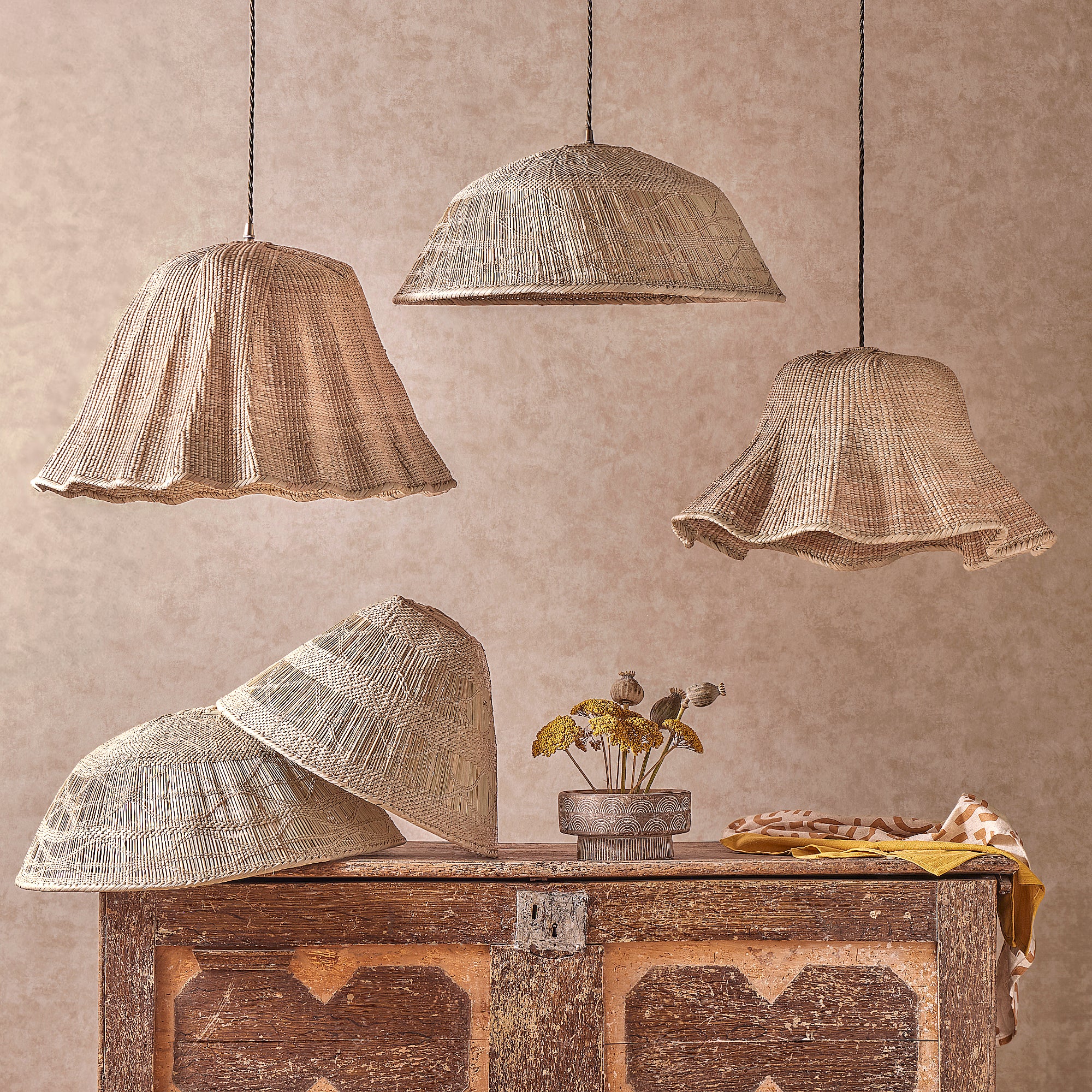 handwoven lampshades hanging from a ceiling above a dresser with a yellow table cloth and flowers