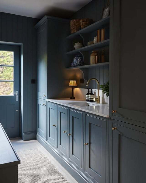 A blue kitchen with shelves and a table lamp next to a marble sink