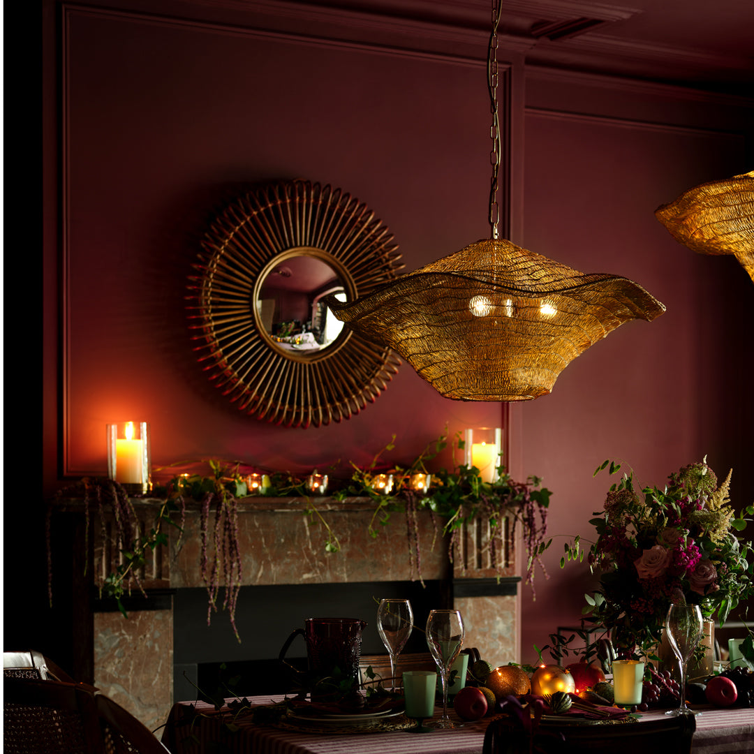 alt:Dimly lit dining room with a woven pendant light, circular mirror, candles on the fireplace mantel, and a table set with flowers.