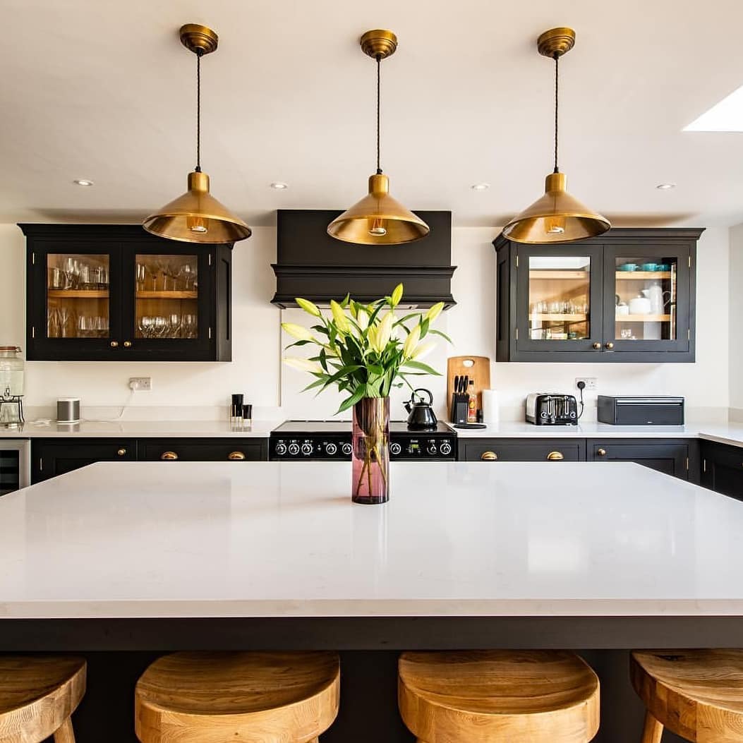 A black and white kitchen with a large centre island. Over the kitchen island there are three hanging brass pendant lights.
