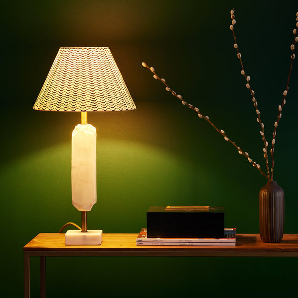 A white marble table lamp on a wooden desk with a black and white shade.